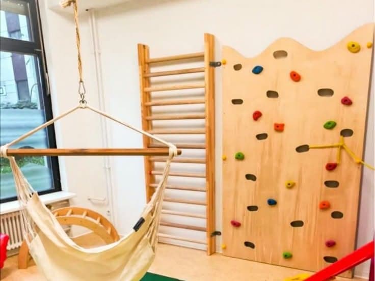 Hängesitz über einer grünen Matte, dahinter Sprossenwand und Kletterwand aus Holz