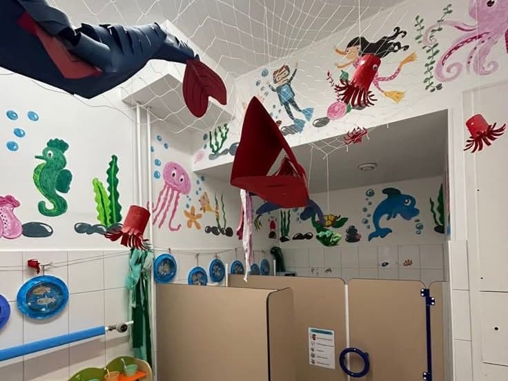 Waschraum mit Kindertoiletten, gemalten Meerestieren an den Wänden und einem Netz unter der Decke