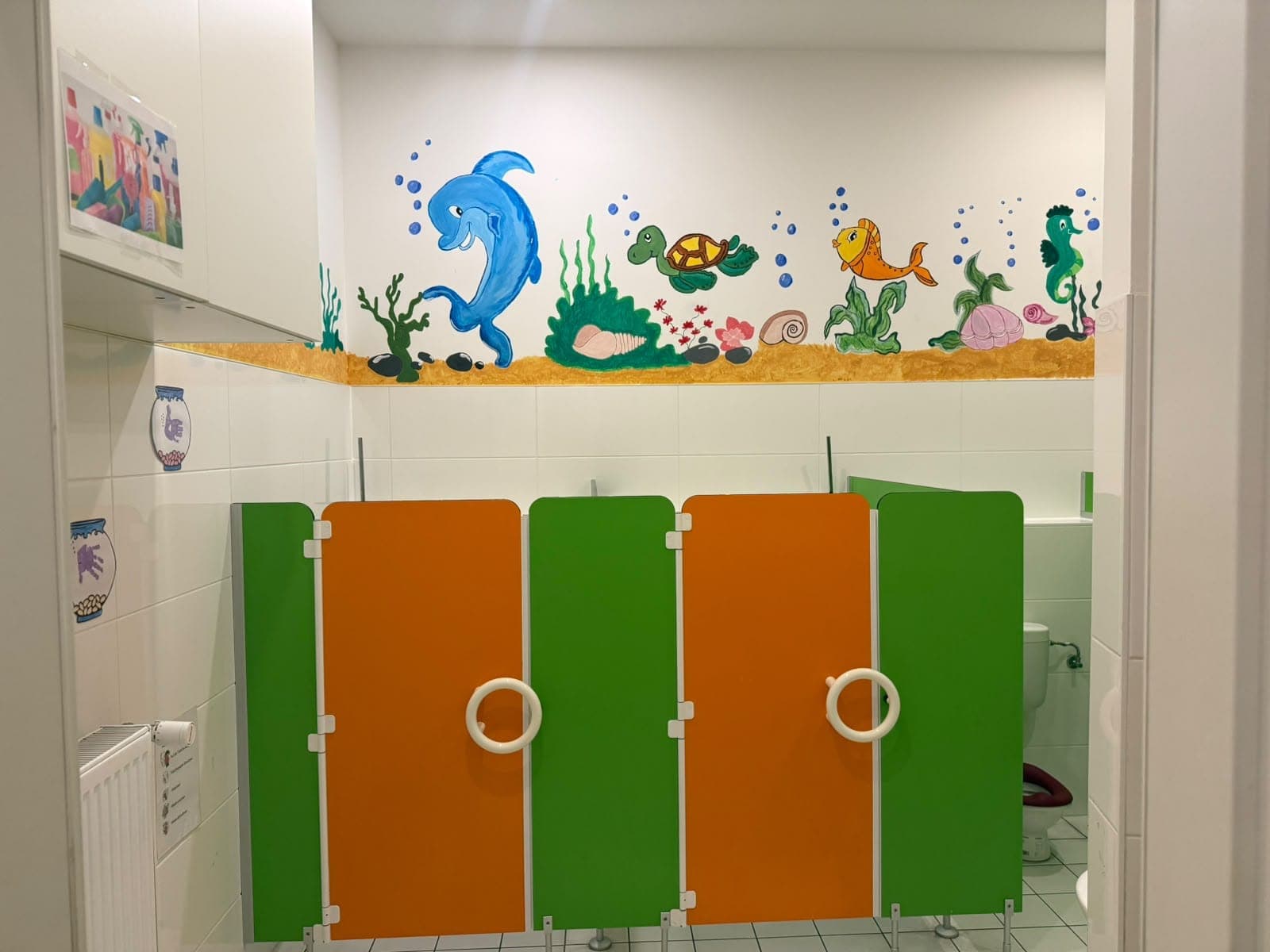 Waschraum mit kleinen Kindertoiletten, darüber ein gemaltes Unterwasserbild mit Delfin und Schildkröte